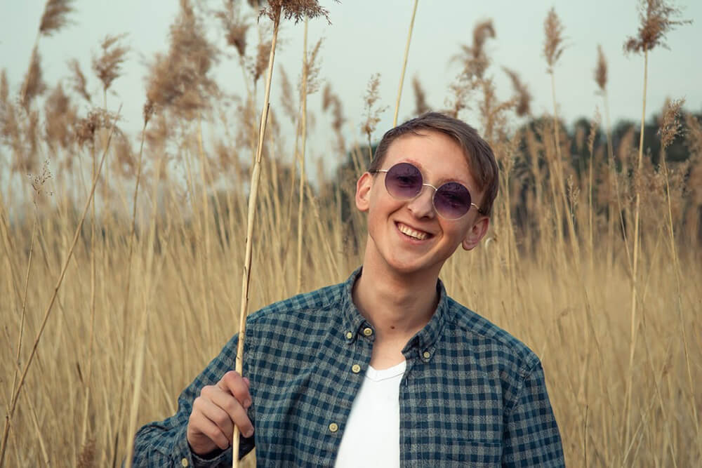 Man standing in a wheat field wearing round trendy sunglasses for men.